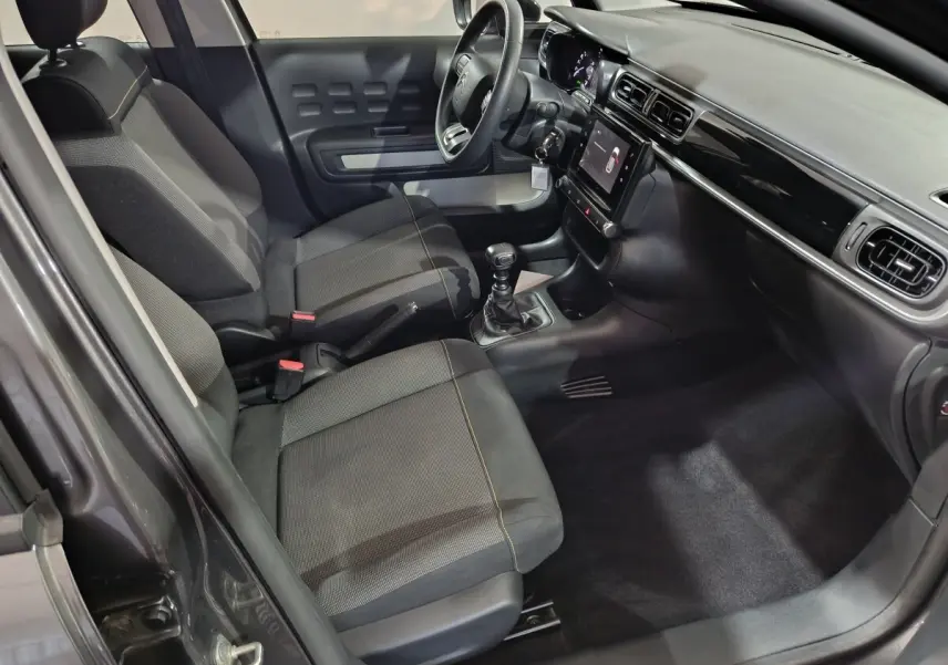 Vue intérieure côté conducteur de la Citroën C3 2024 gris foncé, montrant sièges tissu, volant multifonctions et écran tactile central.
