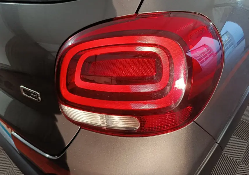 Gros plan sur le feu arrière droit rouge et blanc d'une Citroën C3 gris foncé, avec logo C3 visible sur la carrosserie.