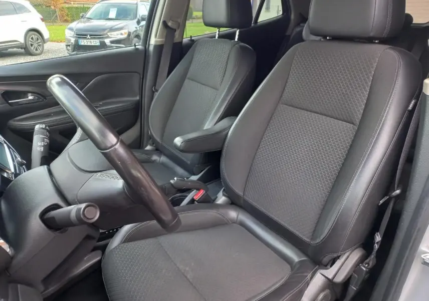 Vue intérieure côté conducteur de l’Opel Mokka X 2017, sièges noirs en tissu et cuir avec accoudoir central.