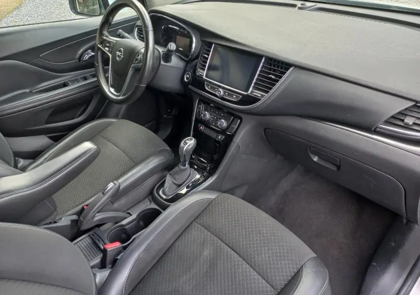 Vue intérieure côté conducteur de l’Opel Mokka X 2017, montrant tableau de bord noir et console centrale avec boîte automatique.