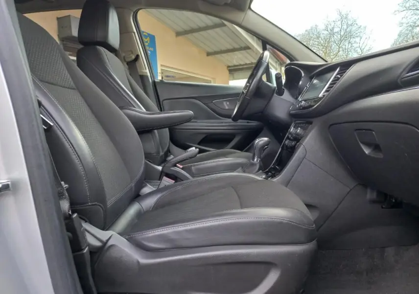 Vue intérieure côté conducteur de l’Opel Mokka X gris 2017, montrant sièges en cuir noir et tableau de bord moderne.