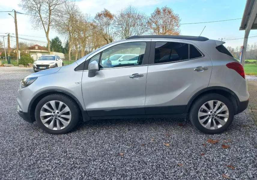 Vue de profil côté gauche d'un Opel Mokka X gris 2017 garé sur un sol gravillonné avec des jantes alliage.