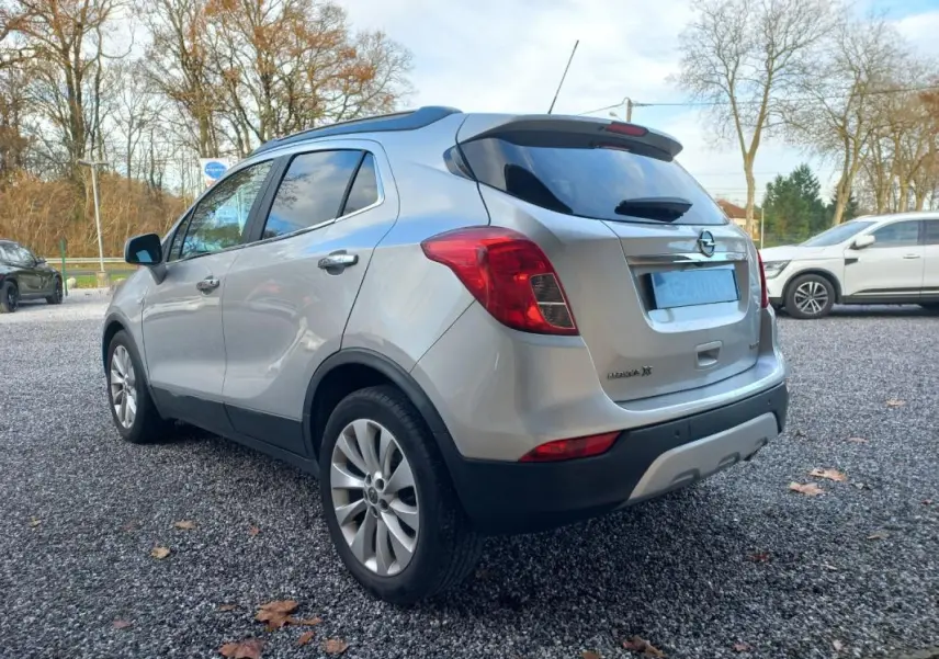 Opel Mokka X gris vue 3/4 arrière côté gauche, avec feux arrière rouges et jantes alliage visibles.