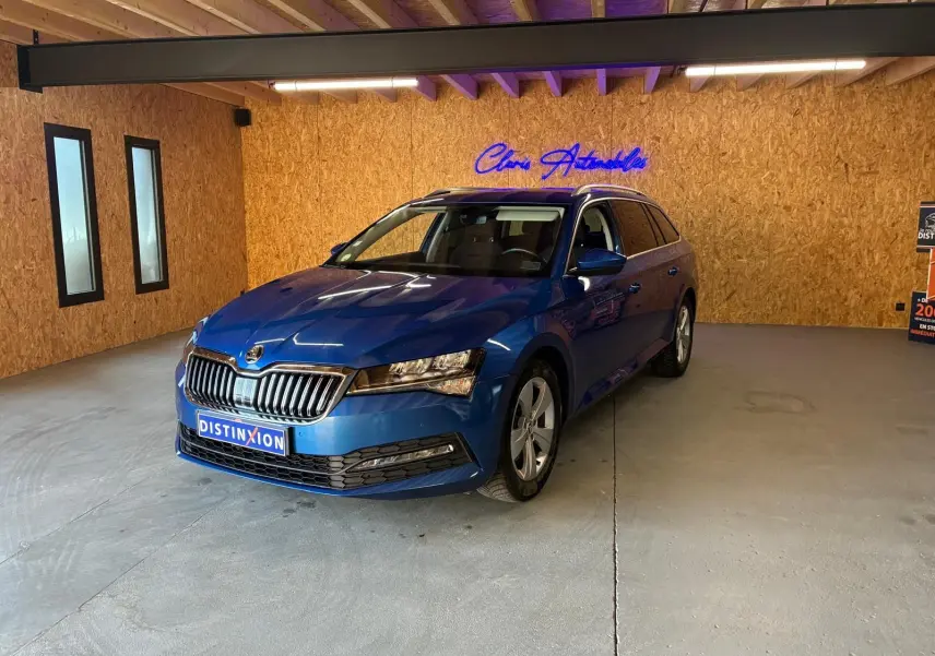 Vue 3/4 avant droite d'une Skoda Superb Combi bleu métallisé dans un showroom avec éclairage intérieur et mur en bois.