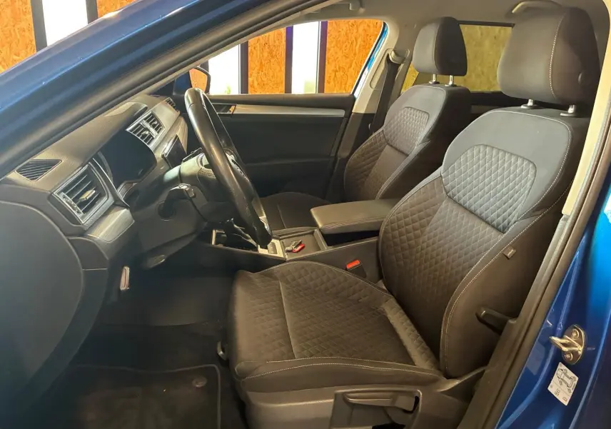 Vue intérieure côté conducteur d'une Skoda Superb Combi bleu 2021, sièges tissu noir avec surpiqûres et tableau de bord moderne.