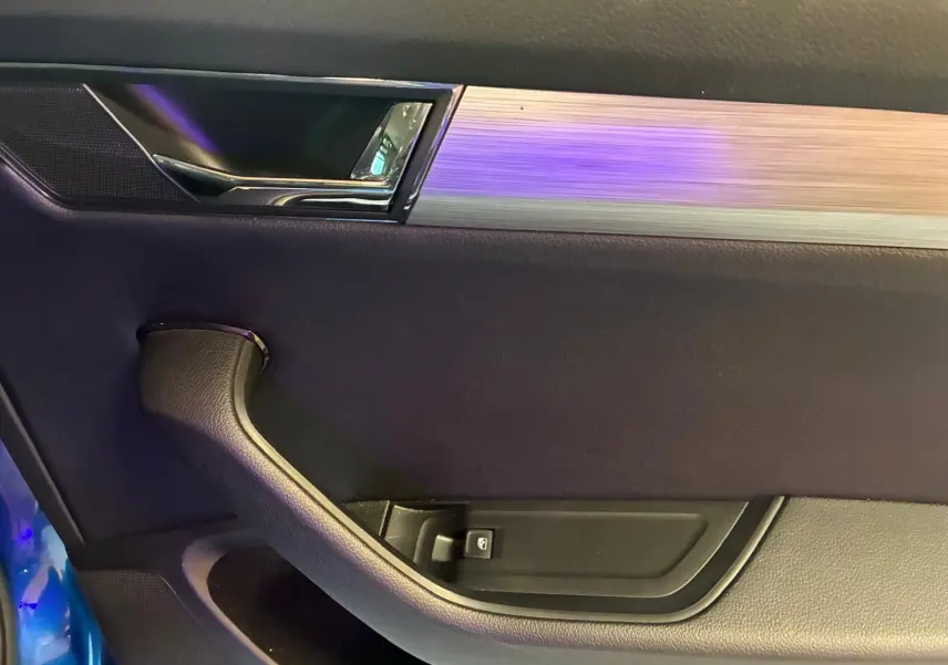 Intérieur côté gauche de la porte d’une Skoda Superb Combi bleu, avec poignée noire et insert aluminium brossé.