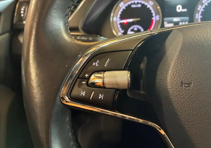 Gros plan sur les commandes gauche du volant noir d’une Skoda Superb Combi 2021 avec tableau de bord numérique en arrière-plan.
