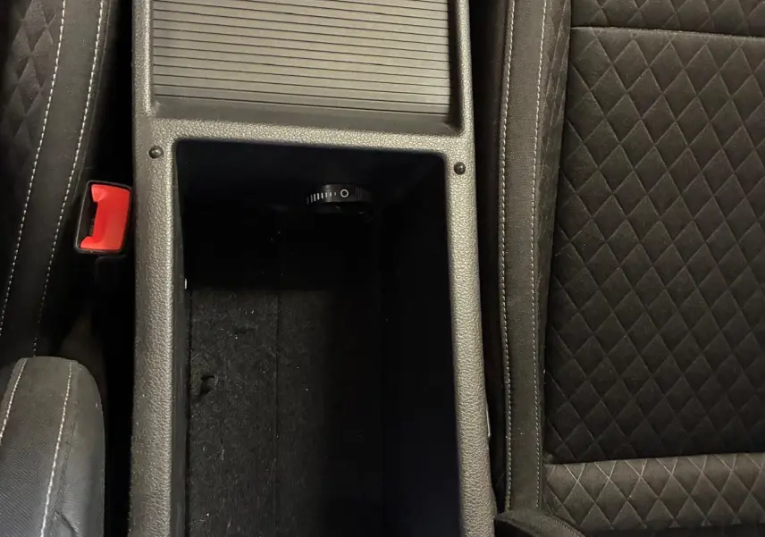 Vue rapprochée de la console centrale noire avec rangement ouvert et sièges tissu noir à surpiqûres blanches dans une Skoda Superb Combi.