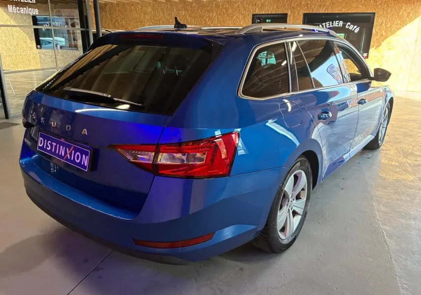 Vue 3/4 arrière droite d'une Skoda Superb Combi bleu métallisé, break diesel 5 portes en intérieur showroom.