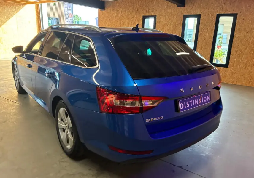 Vue 3/4 arrière gauche d'un break Skoda Superb Combi bleu dans un intérieur avec éclairage naturel.