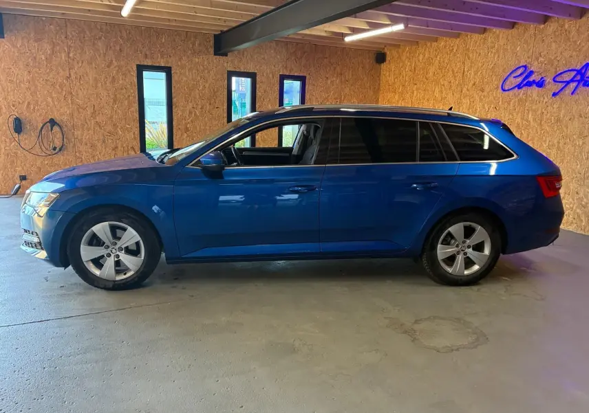 Vue latérale gauche d'une Skoda Superb Combi bleu 2021 stationnée en intérieur avec jantes alliage et vitres teintées.