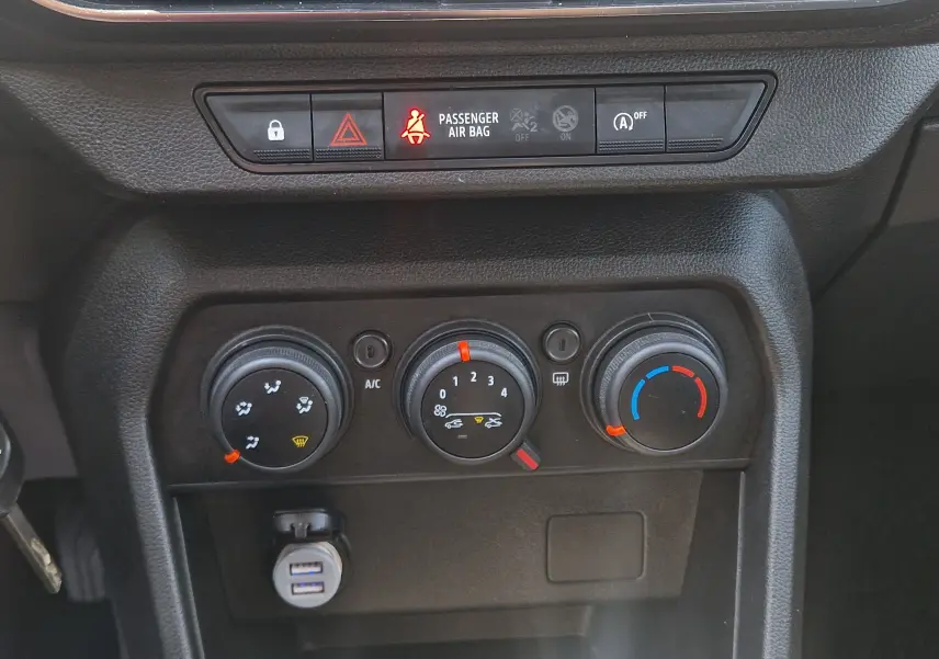 Vue rapprochée du tableau de bord de la Dacia Sandero blanche 2022, montrant les commandes de climatisation manuelle et les voyants lumineux.