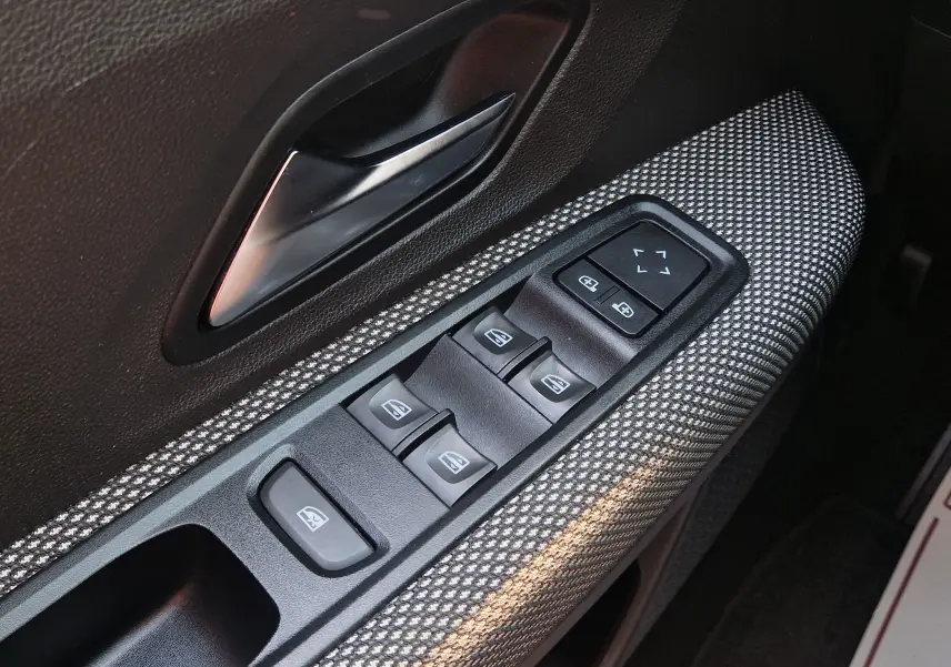 Gros plan sur la commande des vitres électriques côté conducteur d’une Dacia Sandero blanche, tissu gris à motifs.