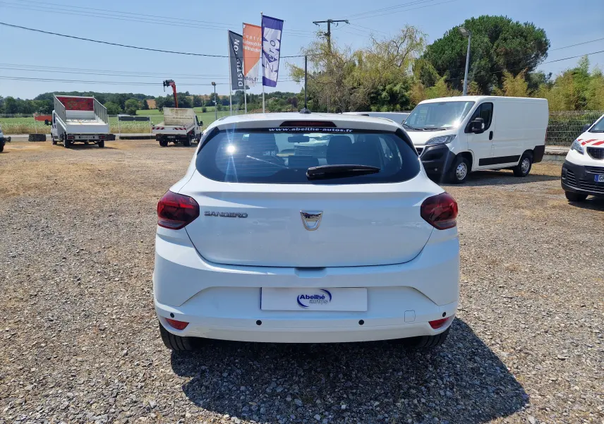 Vue arrière d'une Dacia Sandero blanche 2022, avec feux arrière rouges et logo Dacia visible sur le hayon.