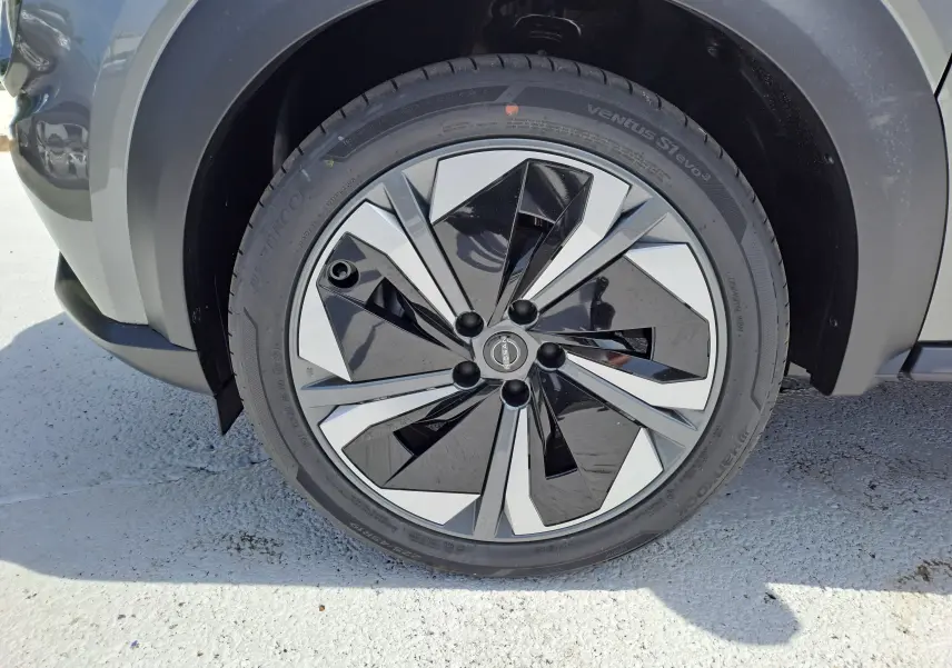 Gros plan sur la roue avant gauche du Nissan Juke Hybrid 143 N-Connecta gris squale avec jante noire et argentée au design géométrique.