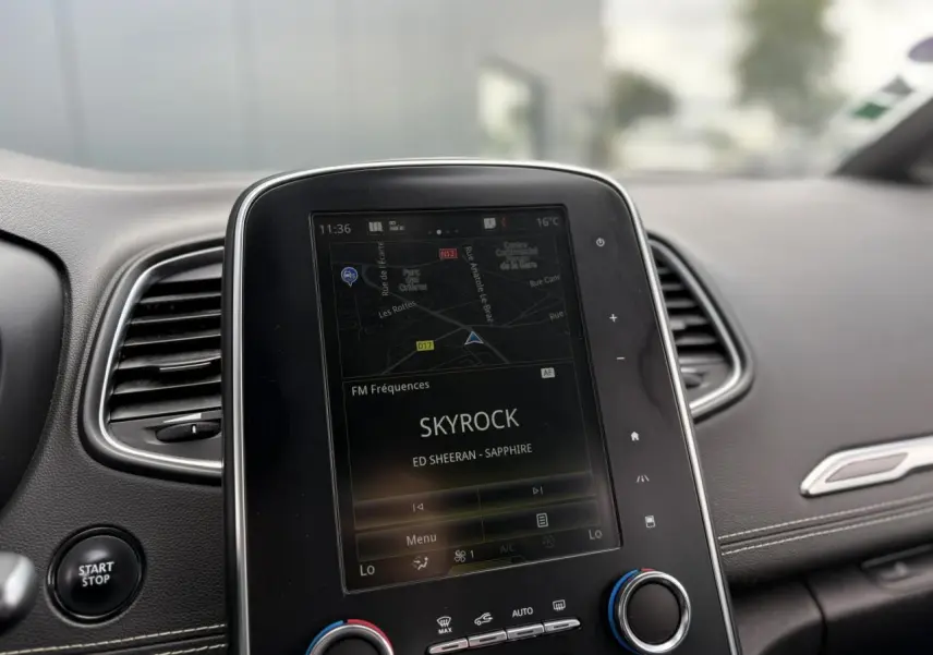 Vue rapprochée de la console centrale du Renault Grand Scenic blanc nacré, écran tactile affichant la radio Skyrock.