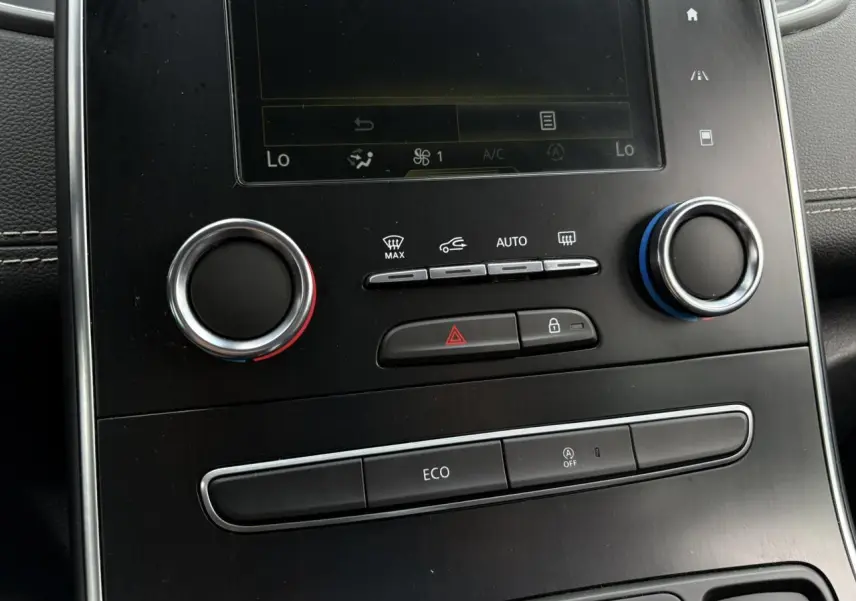 Gros plan sur la console centrale noire du Renault Grand Scenic IV blanc nacré, avec commandes climatisation et bouton Eco visibles.