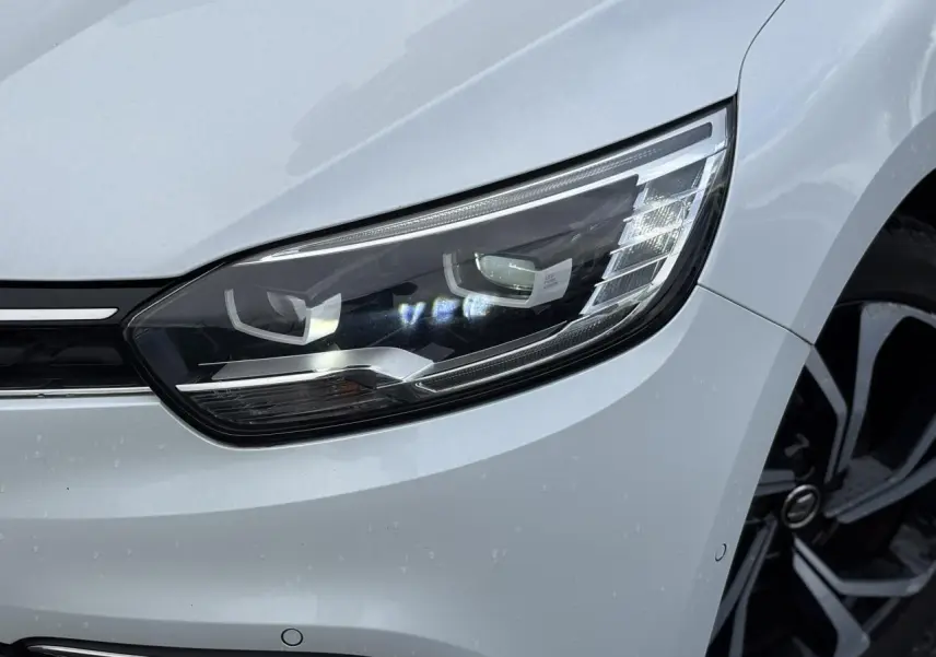 Gros plan sur le phare avant droit blanc nacré du Renault Grand Scenic IV avec jante alliage noire et argentée