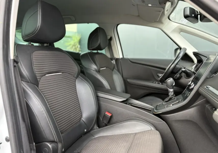 Vue intérieure côté conducteur du Renault Grand Scenic blanc nacré, sièges noirs en cuir et tissu avec console centrale visible.