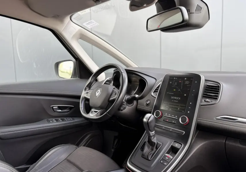 Vue intérieure côté conducteur du Renault Grand Scenic IV avec tableau de bord noir et écran tactile central allumé.
