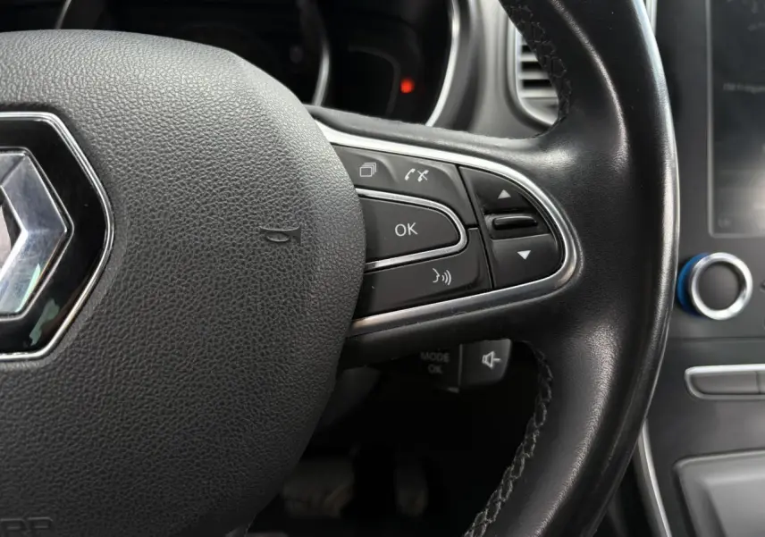 Gros plan sur le volant cuir noir du Renault Grand Scenic IV avec commandes intégrées et logo central chromé.