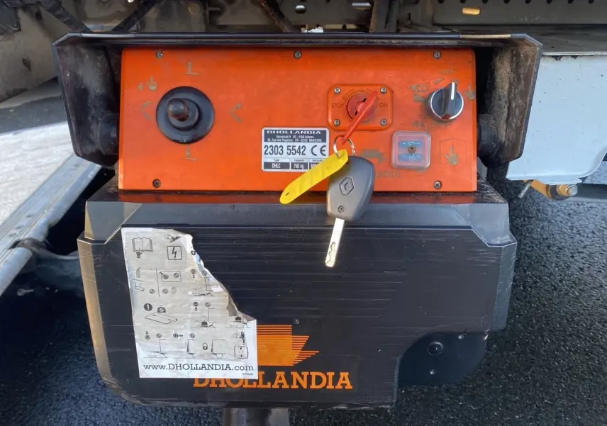 Gros plan sur le boîtier orange du hayon élévateur Dhollandia avec clé Renault accrochée dessous du châssis blanc.