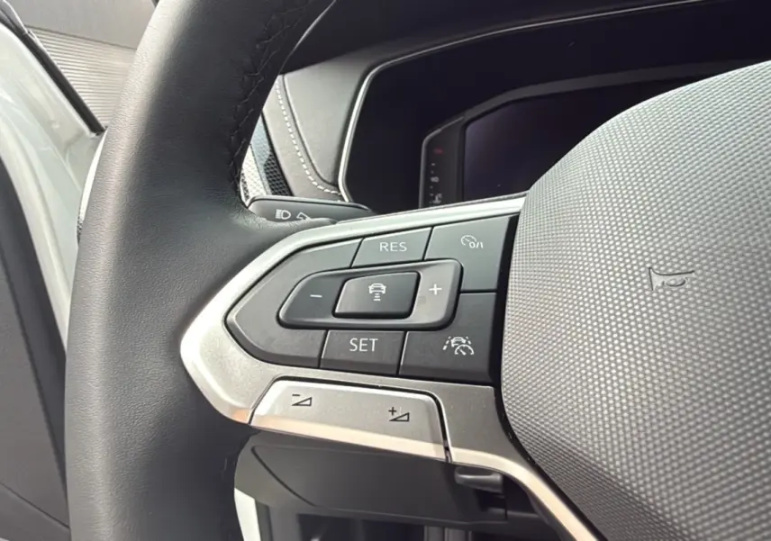 Gros plan sur les commandes multifonctions du volant cuir noir du Volkswagen T-Cross blanc pur 2025.