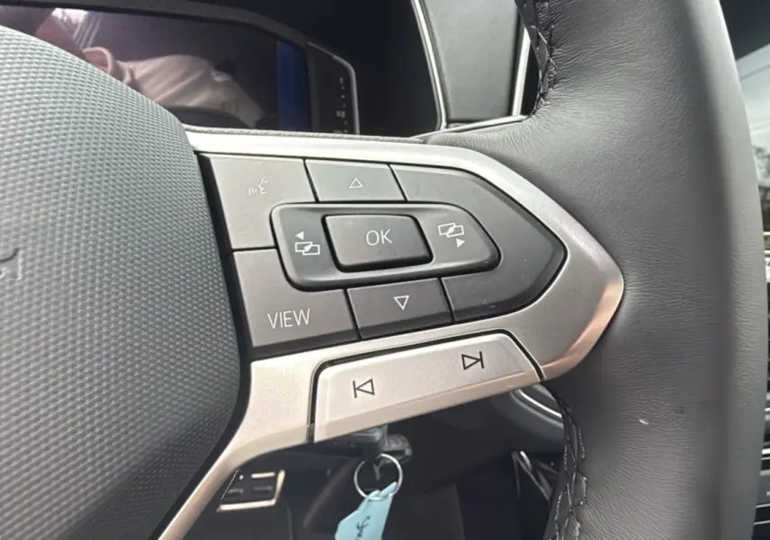 Gros plan sur les commandes multifonctions du volant cuir du Volkswagen T-cross blanc pur, version TSI 116 DSG7 R-LINE 2025.