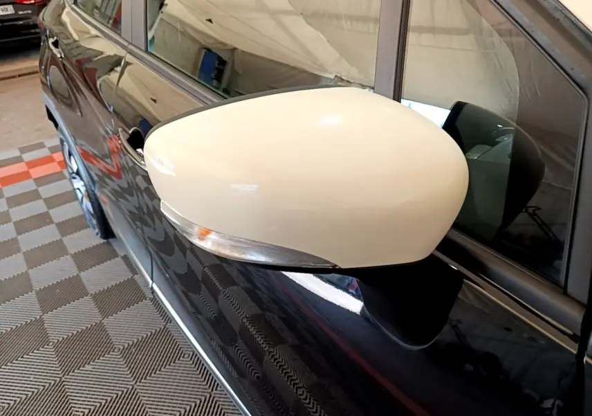 Rétroviseur blanc en gros plan côté gauche d’un Renault Captur noir, reflet de l’environnement intérieur visible.