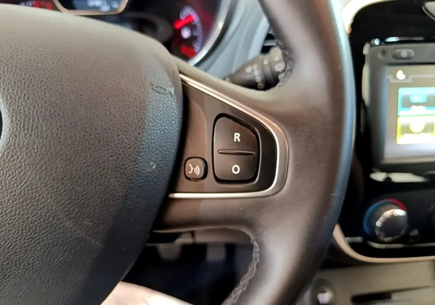 Gros plan sur le volant cuir noir du Renault Captur Business 2018 avec commandes vocales et écran tactile partiel en arrière-plan.