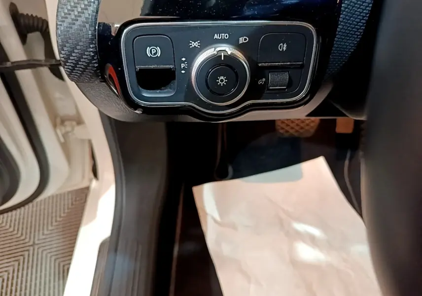 Gros plan sur le panneau de commande des feux et du frein de stationnement d'une Mercedes Classe A blanche, vue côté conducteur.