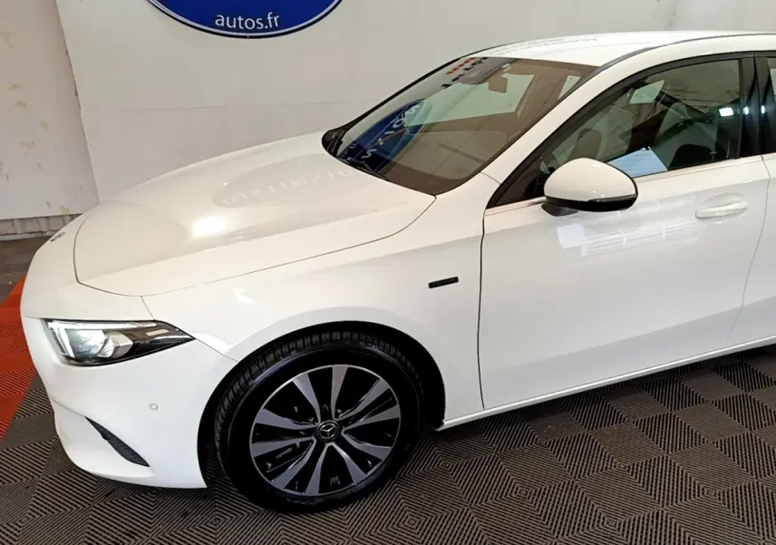 Vue 3/4 avant droit d'une Mercedes Classe A Berline A 250 e Business Line blanche avec jantes noires distinctives.