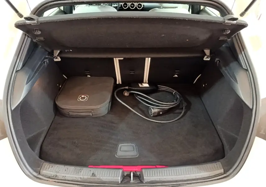 Vue intérieure du coffre ouvert d'une Mercedes Classe A Berline blanche, avec câble de recharge et sac de rangement.