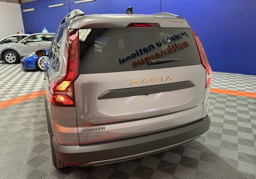 Vue arrière du Dacia Jogger gris schiste métal avec feux allumés dans un showroom intérieur.