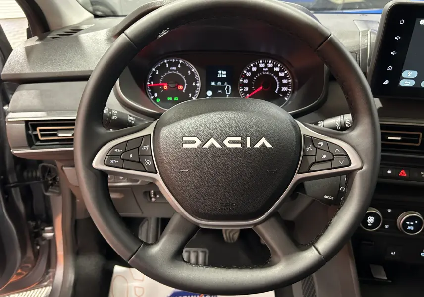 Vue rapprochée du volant noir de la Dacia Jogger gris schiste, avec tableau de bord et commandes visibles.