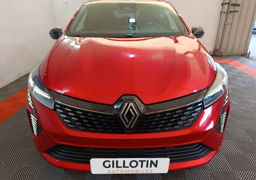 Vue avant d'une Renault Clio Techno TCe 90 rouge 2024 avec calandre noire et feux LED allumés en intérieur.