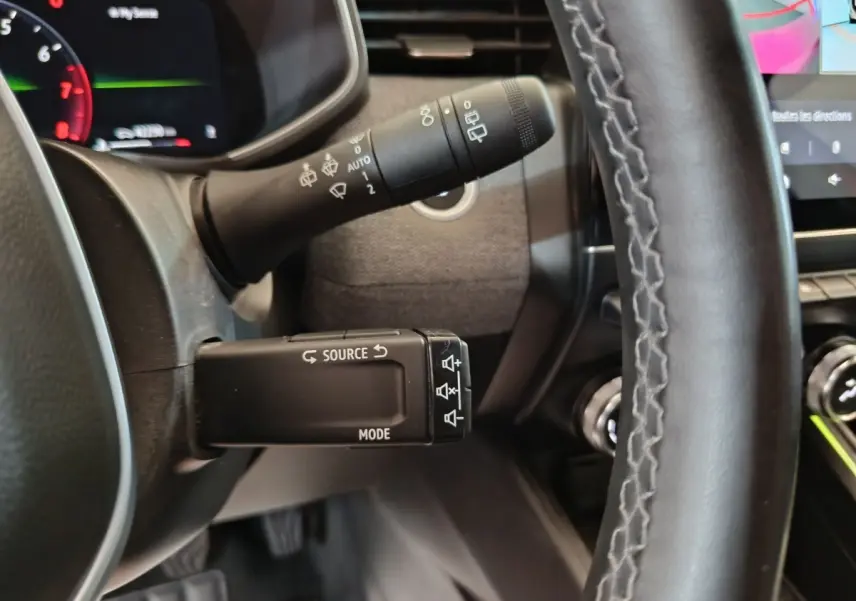 Gros plan sur la manette multifonctions à gauche du volant de la Renault Clio rouge 2024, avec tableau de bord partiellement visible.