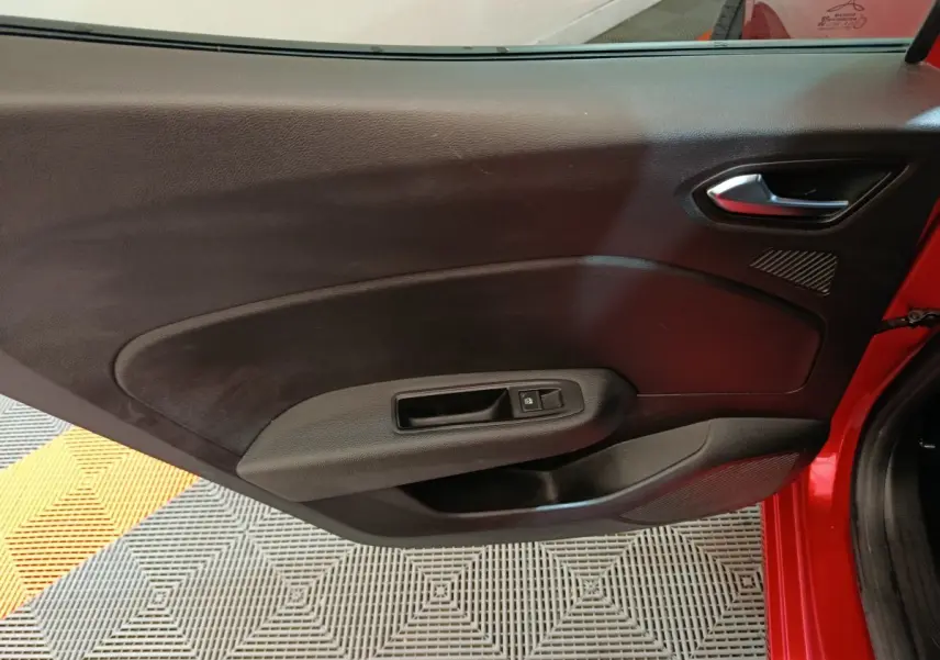 Vue intérieure de la porte avant droite rouge de la Renault Clio 2024 avec poignée et commande de vitre électrique.