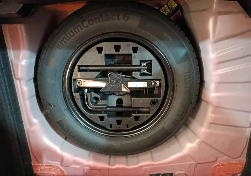 Roue de secours avec outils intégrés dans le coffre d'une Renault Clio rouge 2024, vue de dessus.
