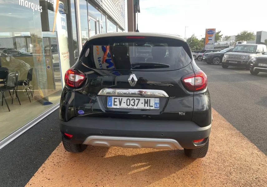 Vue arrière d'un Renault Captur noir étoile avec détails chromés et feux arrière allumés sur parking extérieur.
