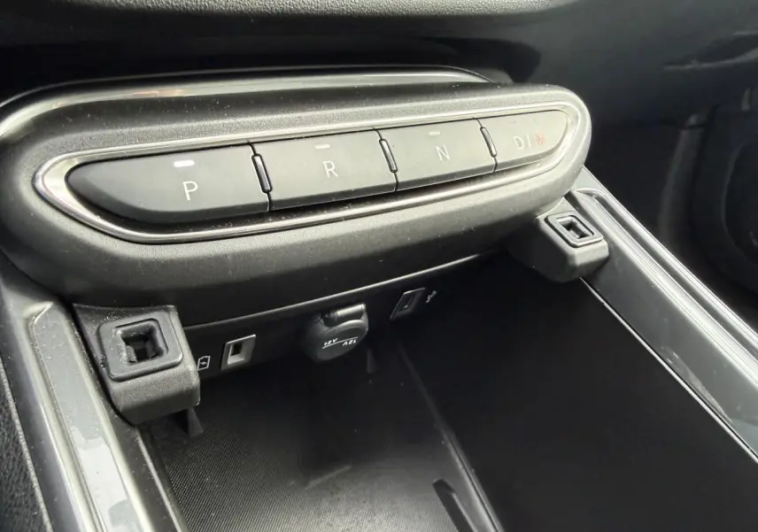 Gros plan sur la console centrale noire du Fiat 600 La Prima 2024, avec boutons de boîte auto et prises USB visibles.