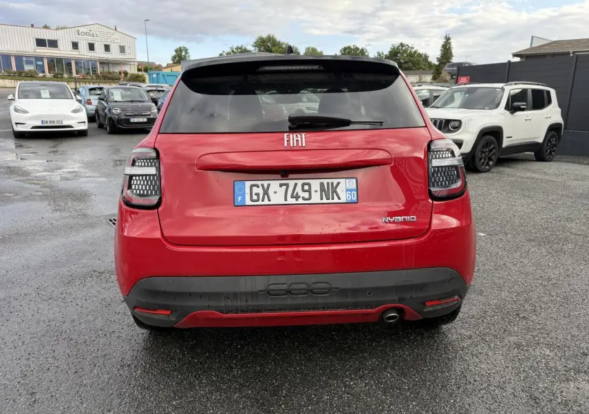 Vue arrière d'une FIAT 600 rouge 2024 avec feux arrière LED et logo Hybrid sur un parking humide.