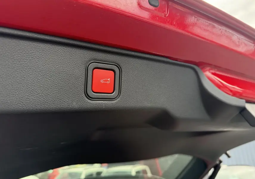 Bouton rouge d'ouverture électrique du hayon sur le bord intérieur du coffre d'une FIAT 600 rouge 2024.