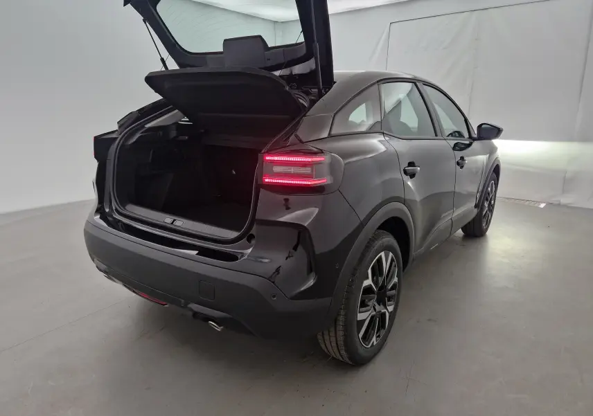 Vue 3/4 arrière droite d'une Citroën C4 noire 2025 avec coffre ouvert et feux arrière allumés dans un studio.