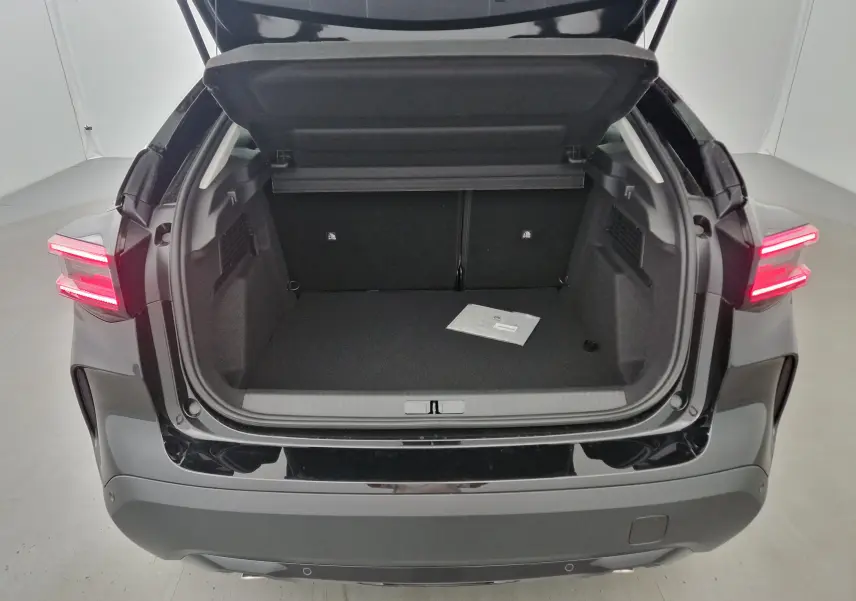 Coffre ouvert vu de l'arrière d'une Citroën C4 noire 2025 avec feux arrière allumés dans un studio blanc.