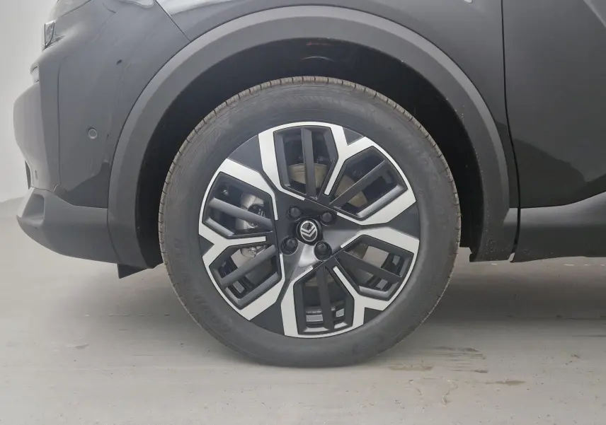 Gros plan sur la roue avant gauche noire d'une Citroën C4 2025, mettant en valeur la jante alu bicolore au design moderne.