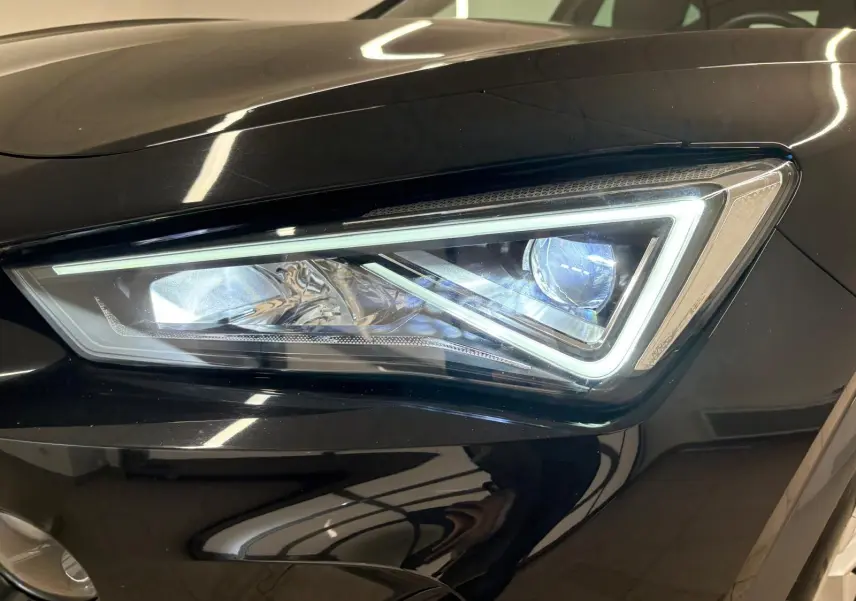 Gros plan sur le phare avant droit allumé du CUPRA Formentor 1.5 TSI noir minuit, soulignant son design anguleux LED.