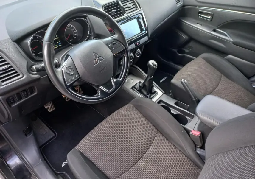 Vue intérieure côté conducteur du Mitsubishi ASX 2020 noir, montrant le volant, la boîte manuelle et l'accoudoir central.