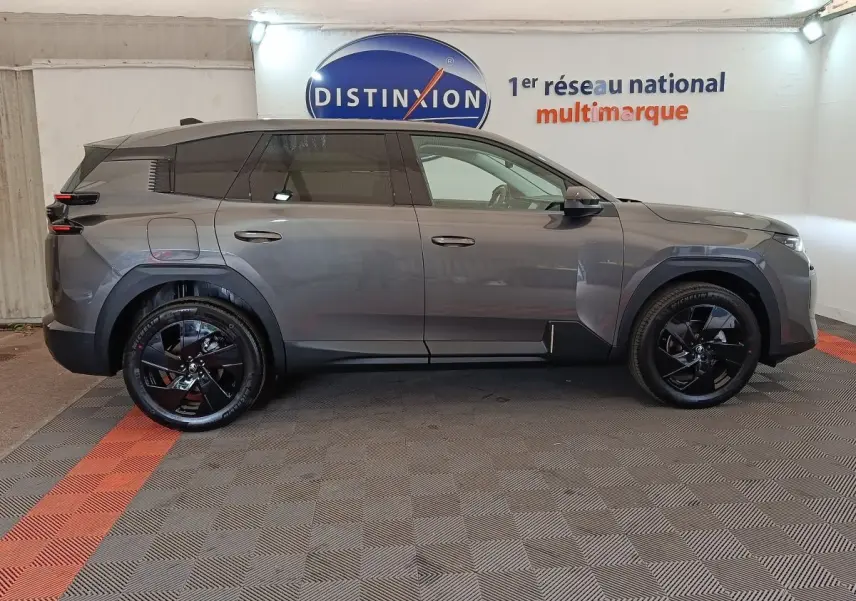 Vue de profil côté gauche d'une Citroën C5 hybride gris foncé avec jantes noires brillantes en intérieur showroom.
