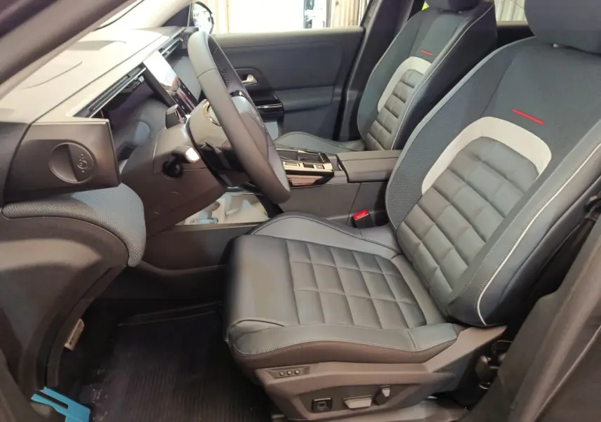 Vue intérieure côté conducteur de la Citroën C5 Hybride 2026 avec sièges cuir gris et détails rouges sur appuie-tête.